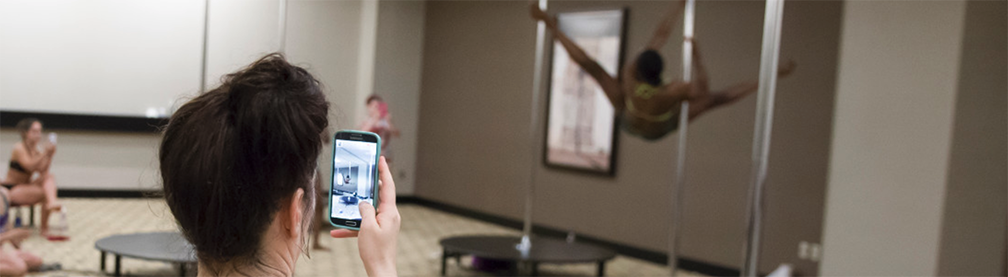 Person takes a picture of a PoleCon attendee demonstrating a Pole Dancing straddle.