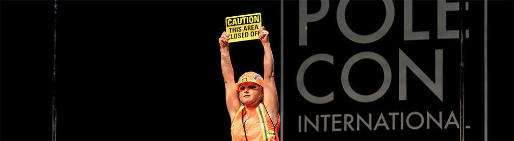 Pole dancer in hard hat with caution sign dances on stage.