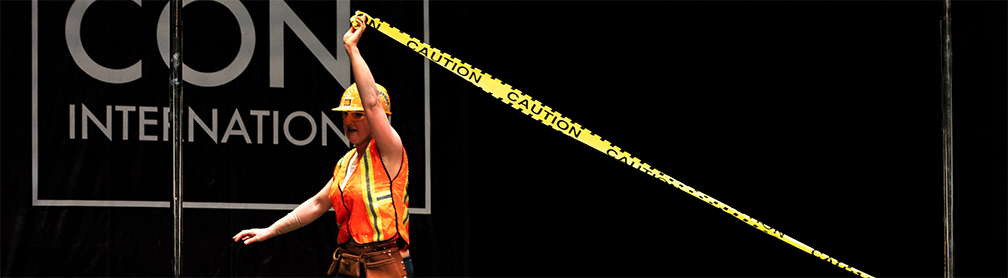Pole dancer in hard hat with caution tape dances on stage.