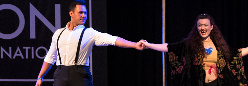 Man And Woman Dance In Front Of A Pole On The PoleCon Stage.